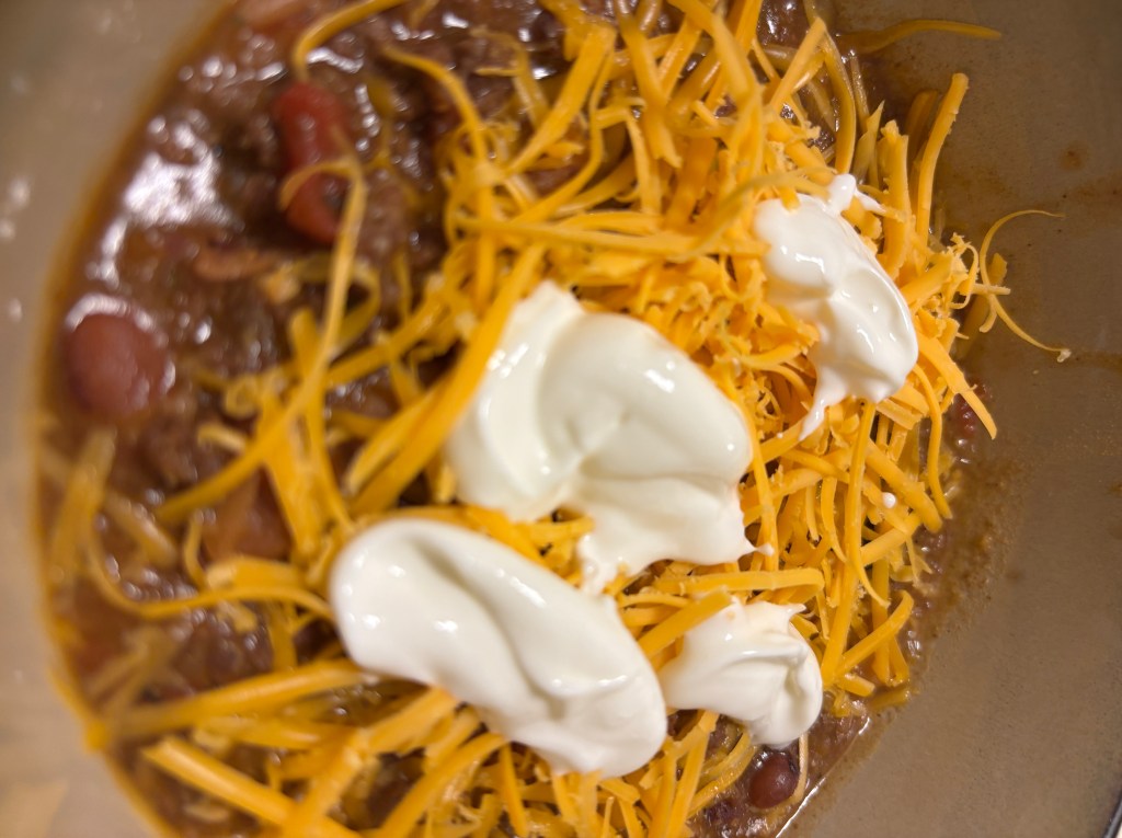 Bowl of bacon and two-bean chili topped with shredded cheddar and sour cream