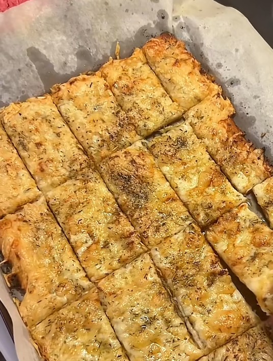 Homemade East Coast garlic fingers with melted cheese and herbs, cut into strips on parchment