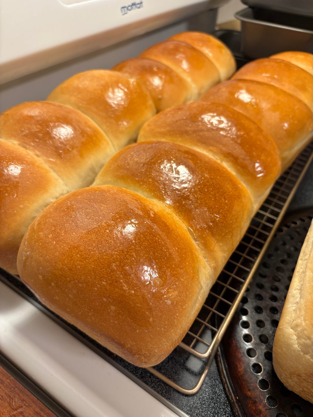 Two pans of glazed homemade white bread rolls cooling on a rack