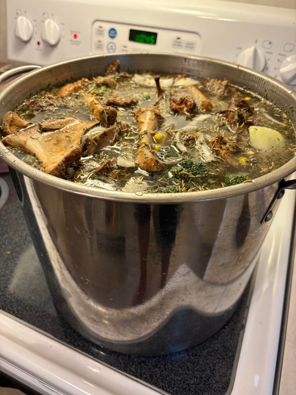 Big stock pot of chicken bone stock simmering with roasted bones, onion, corn and herbs